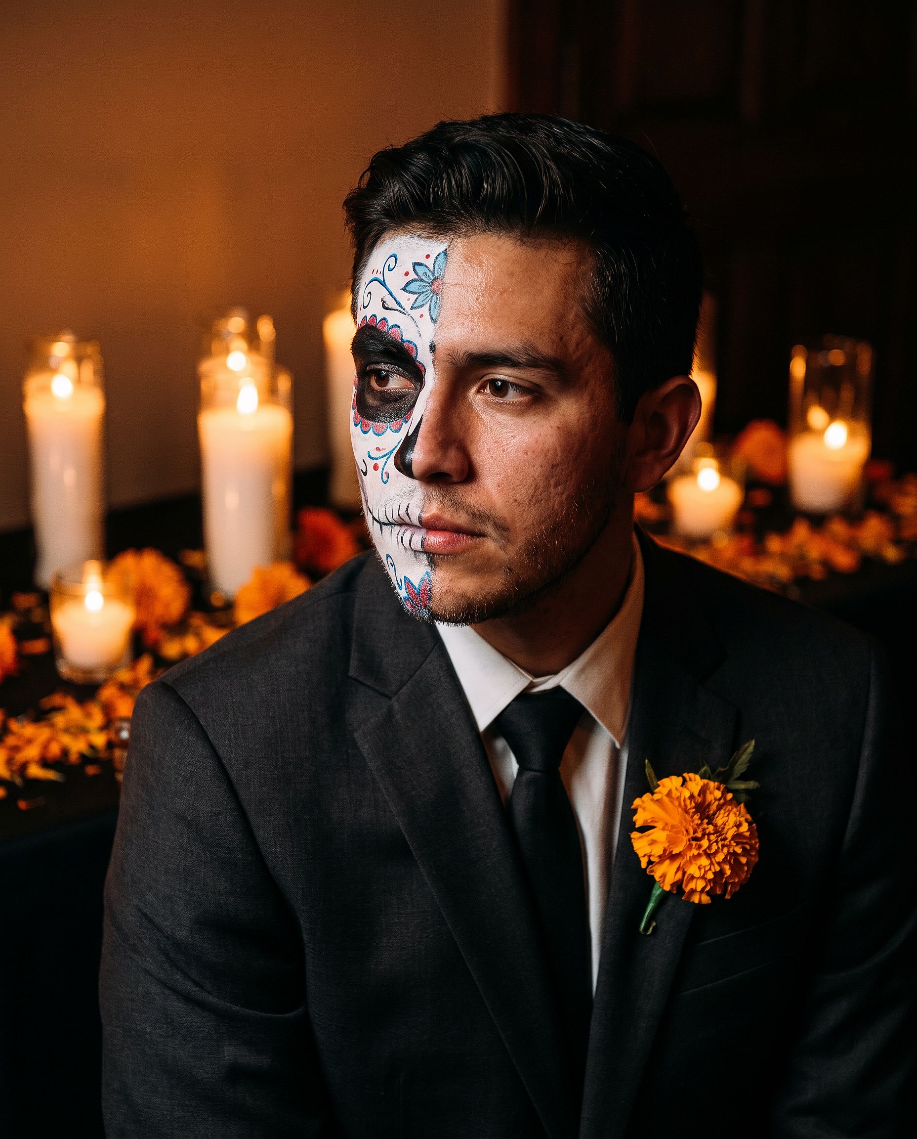 a man with half-face sugar-skull Halloween makeup against a candlelit marigold background