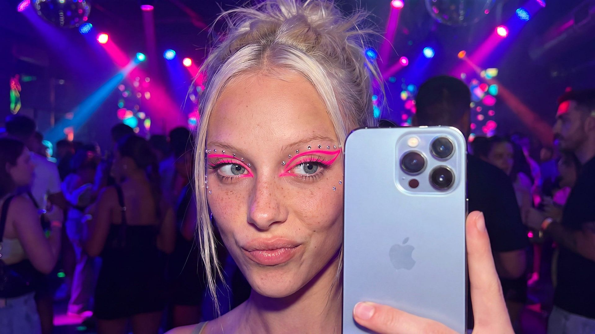 After: Instagram-style party selfie with neon pink eyeliner and rhinestones under club lights