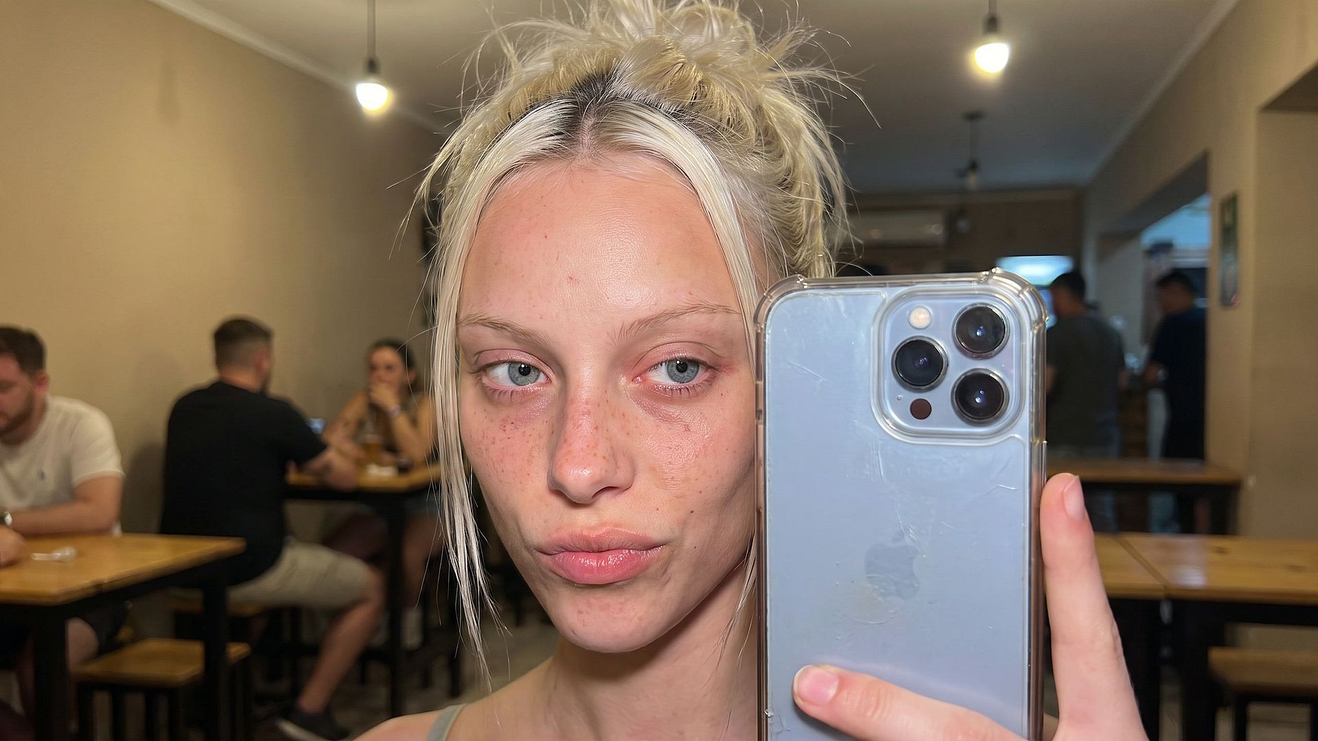 Before: unedited selfie with no makeup in a plain, dimly lit bar