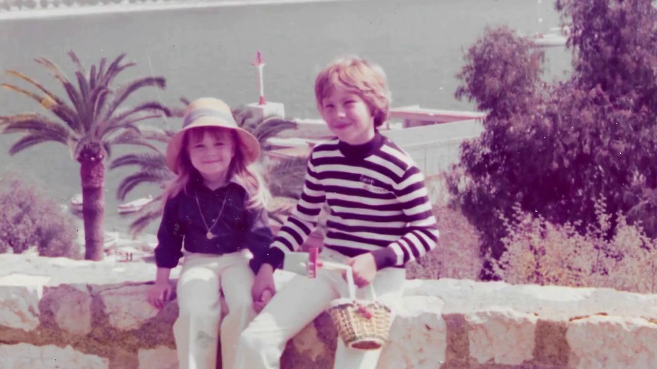 Prompt: Create a video of me and my sister walking to the wall and sit to take a pose for this picture.