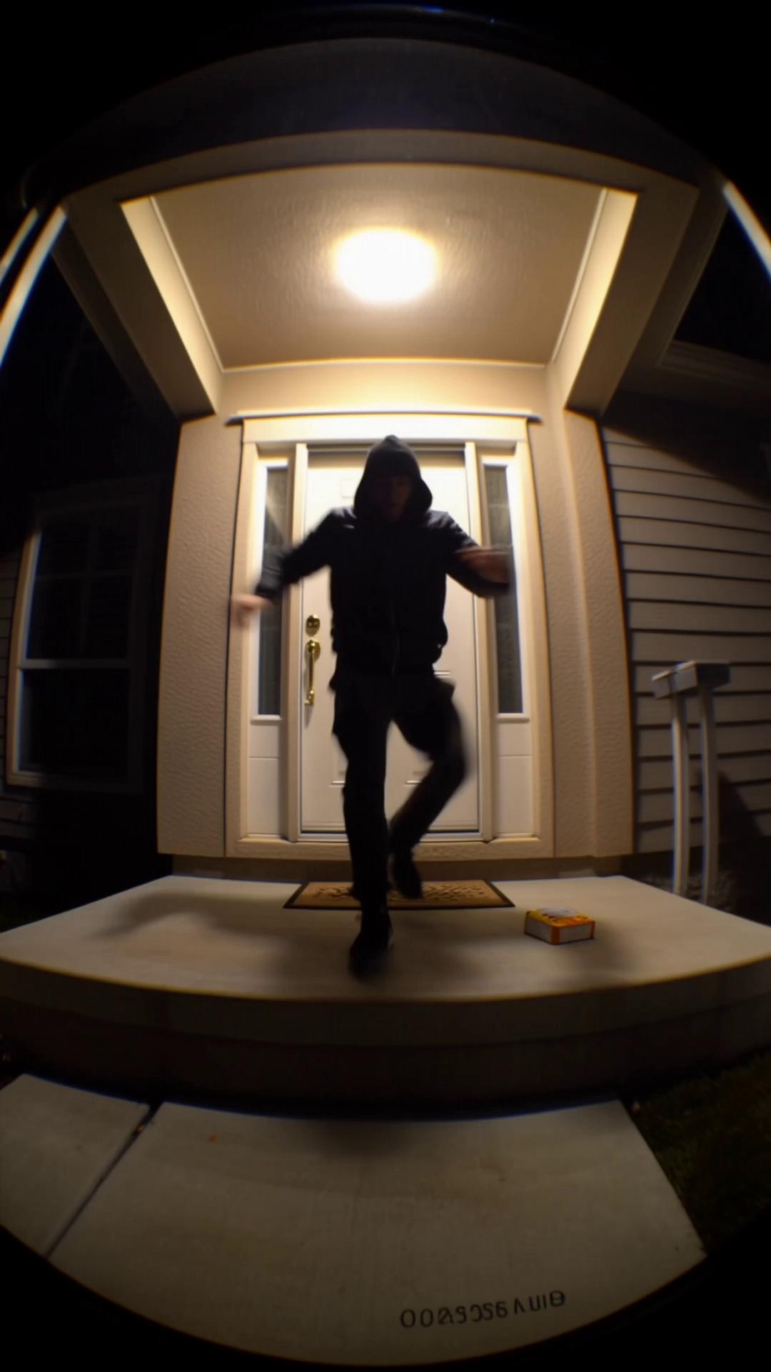 Prompt: Subject: A hooded guy, face partially hidden, wearing dark casual clothes.
Composition: Doorbell camera point of view, wide-angle lens, slight fisheye distortion, medium-to-wide shot from a low angle, typical Ring doorbell perspective.
Action: The hooded guy rushes onto the porch, grabs a delivered package, looks around nervously, then unexpectedly sits down on the front steps. He opens the package on the spot, reveals cat litter inside, freezes in disbelief, slowly looks straight into the doorbell camera, closes the box in frustration, angrily throws it against the front door, and walks away empty-handed.
Location: Residential house front porch at night, suburban setting, visible front door, porch steps, and package placement area.
Style / Aesthetic: Realistic security camera footage, night vision or low-light Ring camera look, slight motion blur, high contrast, surveillance aesthetic, authentic doorbell camera timestamp vibe, cinematic but realistic.