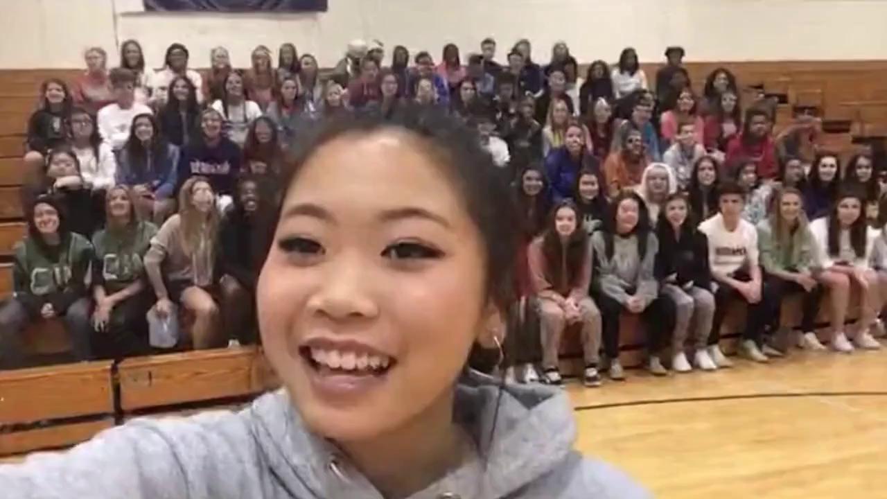 Prompt: a Asian girl is recording herself and a crown of people in the school gym saying, "six seven!'