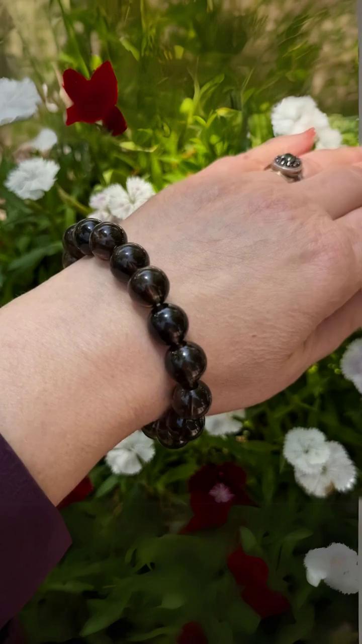 Prompt: A slow camera pan of the arm and hand, with the bracelet kept in focus at all times. The flowers and grass in the background is slowly moving in the slight wind. Everything feels peaceful and easy.