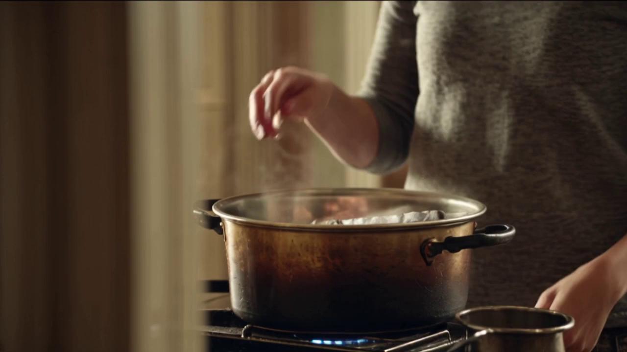 Prompt: a woman stands in a warm, softly lit kitchen, calm and focused. On the stove is a deep, slightly worn pot quietly simmering. She holds a copy of the book Thinking, Fast and Slow by Daniel Kahneman. With intention, she places the book into the pot, letting it slide below the surface. Steam begins to rise gently. She stirs once, then leans in, closes her eyes, and inhales the vapor with a soft smile—as if drawing inspiration from what’s simmering. The moment feels grounded, with a quiet, almost poetic surrealism—like she’s cooking ideas rather than food. No symbols or effects, just rich atmosphere and subtle metaphor.