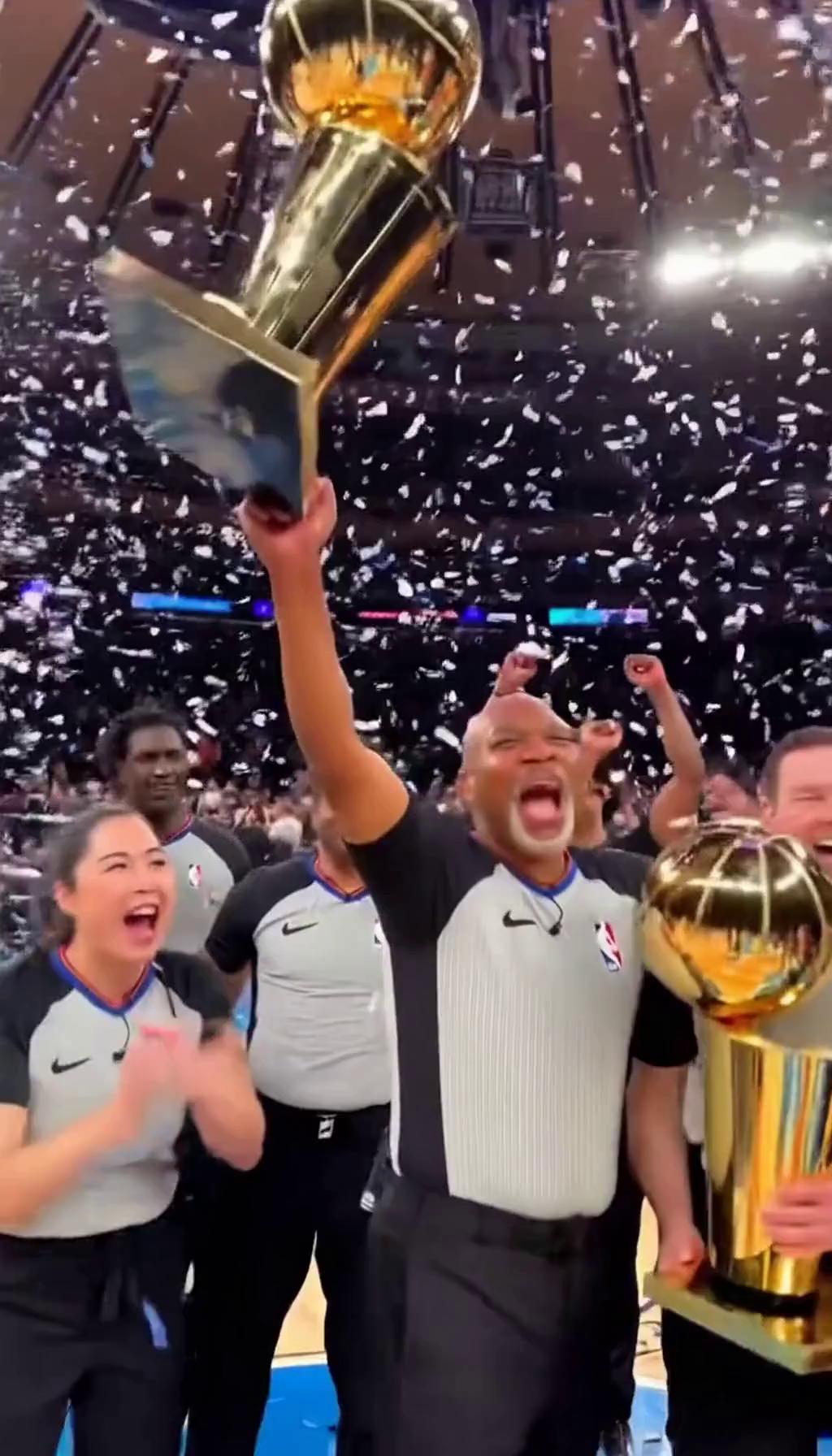 Prompt: An nba referee is holding an NBA finals mvp trophy in one hand, surrounded by celebrating referees. One of the surrounding referees is holding the Larry o brien trophy. White, black, and Grey confetti is falling from the sky. The setting is in Madison Square garden, emulating the atmosphere of the NBA finals, in which the referees have won.