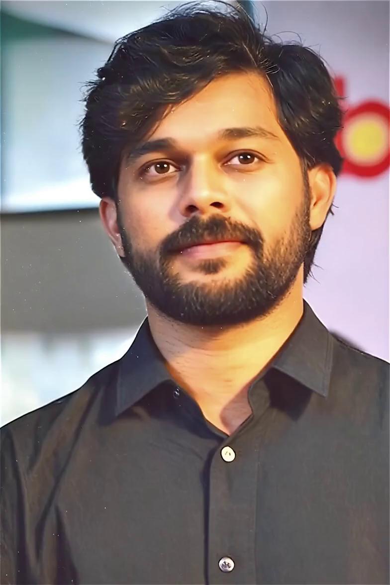 Prompt: use the man face from image i attached . Dark abandoned house interior at night, neon blue shadows filling the space, flickering candles casting sharp neon red highlights, Boss, a late-20s funky gangster wearing a red embroidered oversized jacket, heavy gold chains and rings, walks slowly into frame from deep darkness, his swagger confident and relaxed, gold chains gently swinging, his face half-lit in neon red and half in neon blue, dust particles floating, walls trembling subtly, cinematic horror atmosphere, film grain, volumetric fog, continuation universe