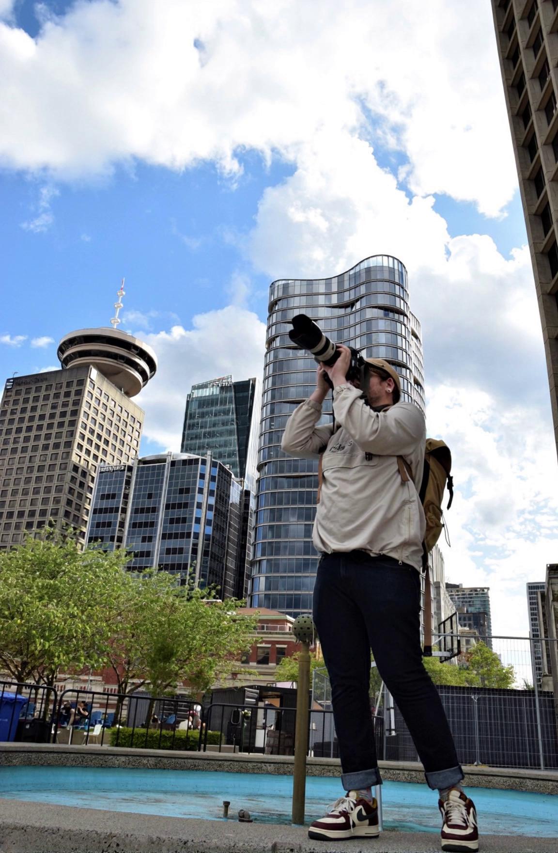 Prompt: dark skies, storm, epic, photographer taking photos while all buildings in the background are exploding and windows are shattered, cool, movie scene, popular Instagram reel