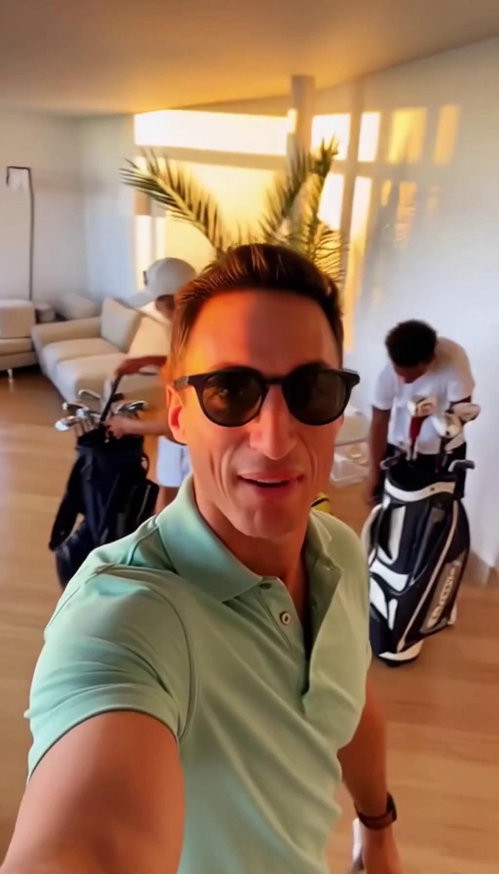 Prompt: A handheld, first-person vlog following a group of friends on a summer golf trip in Turkey: bright morning sun over a coastal championship golf course with palm trees and mountains in the distance, quick cuts of packing golf bags, airport arrival, laughing selfies, and riding golf carts on lush green fairways. The main subject, a relaxed guy in sunglasses and a polo shirt, talks casually to the camera while walking between holes, friends joking in the background. Smooth but slightly shaky vlog camera movement, wide-angle lens, natural colors with warm golden highlights, blue skies and vibrant greens. Action beats include teeing off in slow motion, balls flying against the sky, clinking drinks at a clubhouse terrace, and a sunset shot overlooking the course. Audio includes light wind, distant ocean ambience, golf swings, laughter, and casual spoken commentary, upbeat and carefree travel-vlog mood, realistic modern smartphone footage style.