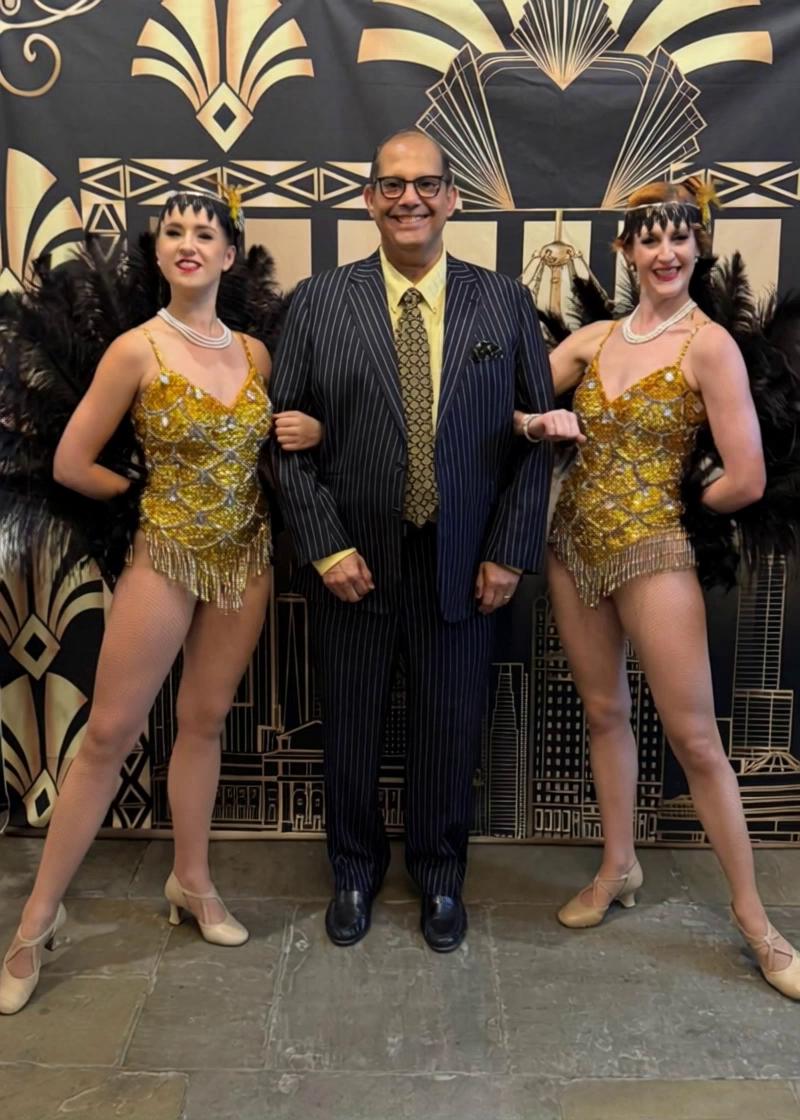 Prompt: The two dancers smile and rub against the man in the middle. He kisses them both and puls them tightly towards himself. Smiles atvthe camera and his tongue lolls out. 