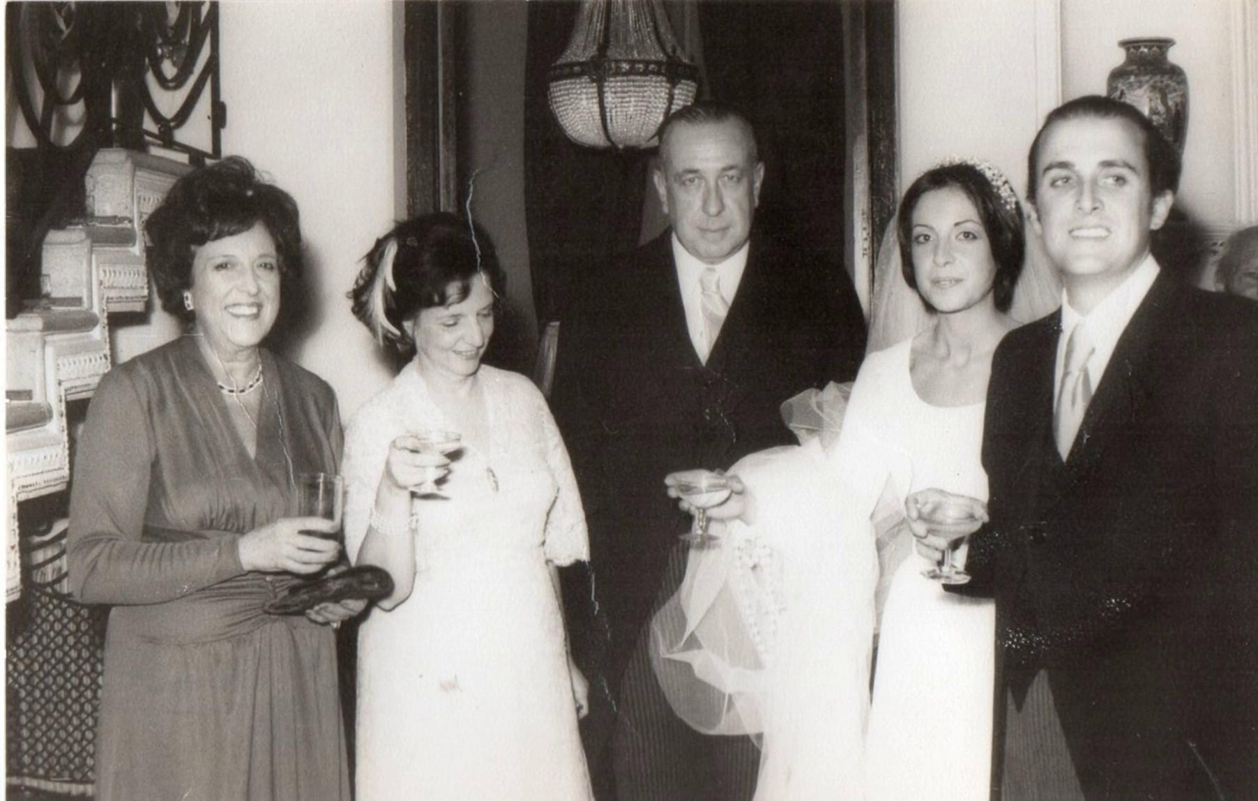 Prompt: Los novios en la fiesta de casamiento brindan con los suegros y luego cortan la torta con mucha gente bien vestida. 