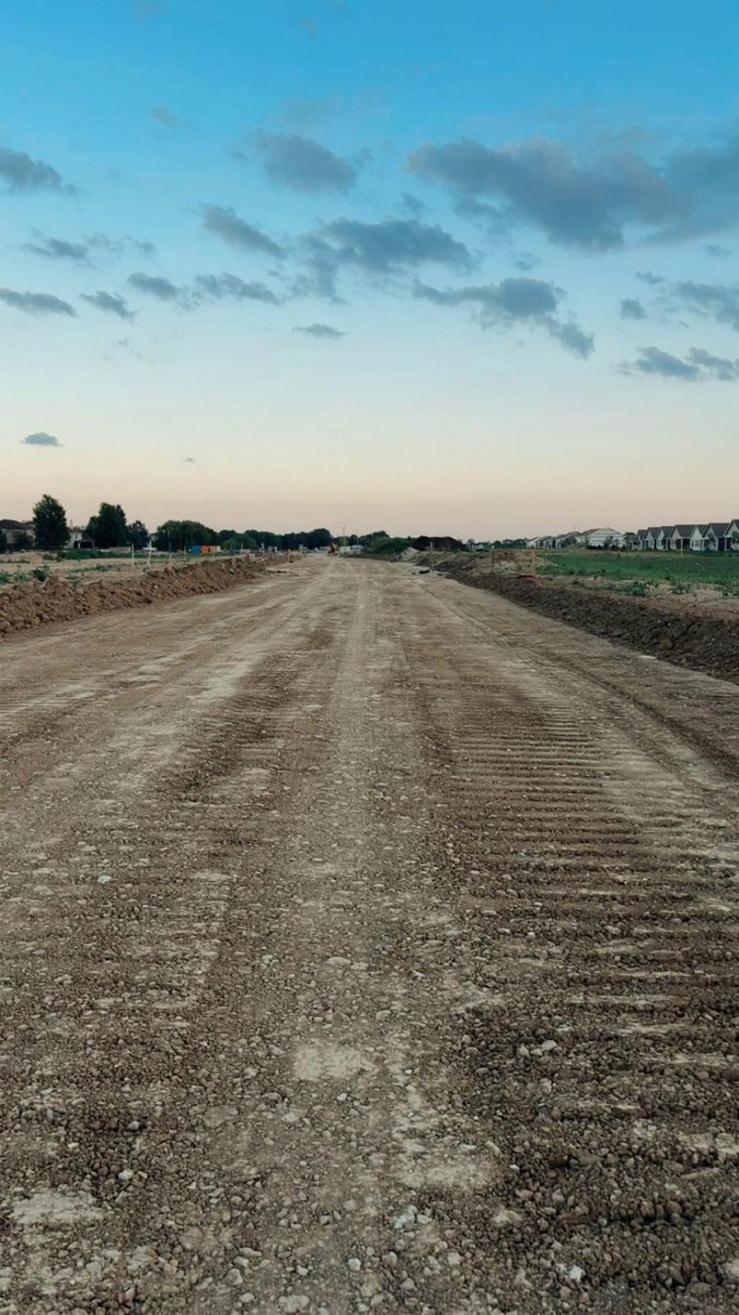 Prompt: Start frame: the provided empty construction land photo with a wide dirt road and open area.End frame: the provided finished apartment building exactly like the reference image. The final building must clearly show the wall text “BERF YAPI” on the upper facade.Create a 100% realistic construction process from the empty land to the completed building.Scene begins with an empty construction site. Survey markers appear. Yellow construction machines arrive: excavators, bulldozers, dump trucks and compactors. Workers wearing helmets and safety vests begin excavation.Excavators dig the foundation while trucks remove soil. The ground is leveled and compacted. Workers install formwork and dense steel rebar reinforcement for the foundation. Concrete mixer trucks arrive and a concrete pump pours concrete into the foundation.Reinforced concrete columns, beams and floor slabs are built step by step. Scaffolding surrounds the structure. Workers continue construction while cranes and lifting machines move materials. Floors are completed one by one.Exterior phase: walls, insulation, plaster and facade paint are applied. Windows and balcony glass railings appear. Roof structure is completed.Final phase: landscaping with grass, paths, trees and flowers appears around the building.Camera moves smoothly around the construction site in a 360-degree orbit during the entire building process. Wide realistic shots, no close-ups.Final frame matches the reference building exactly and the facade text “BERF YAPI” is clearly visible.Ultra realistic workers, machines and construction activity.