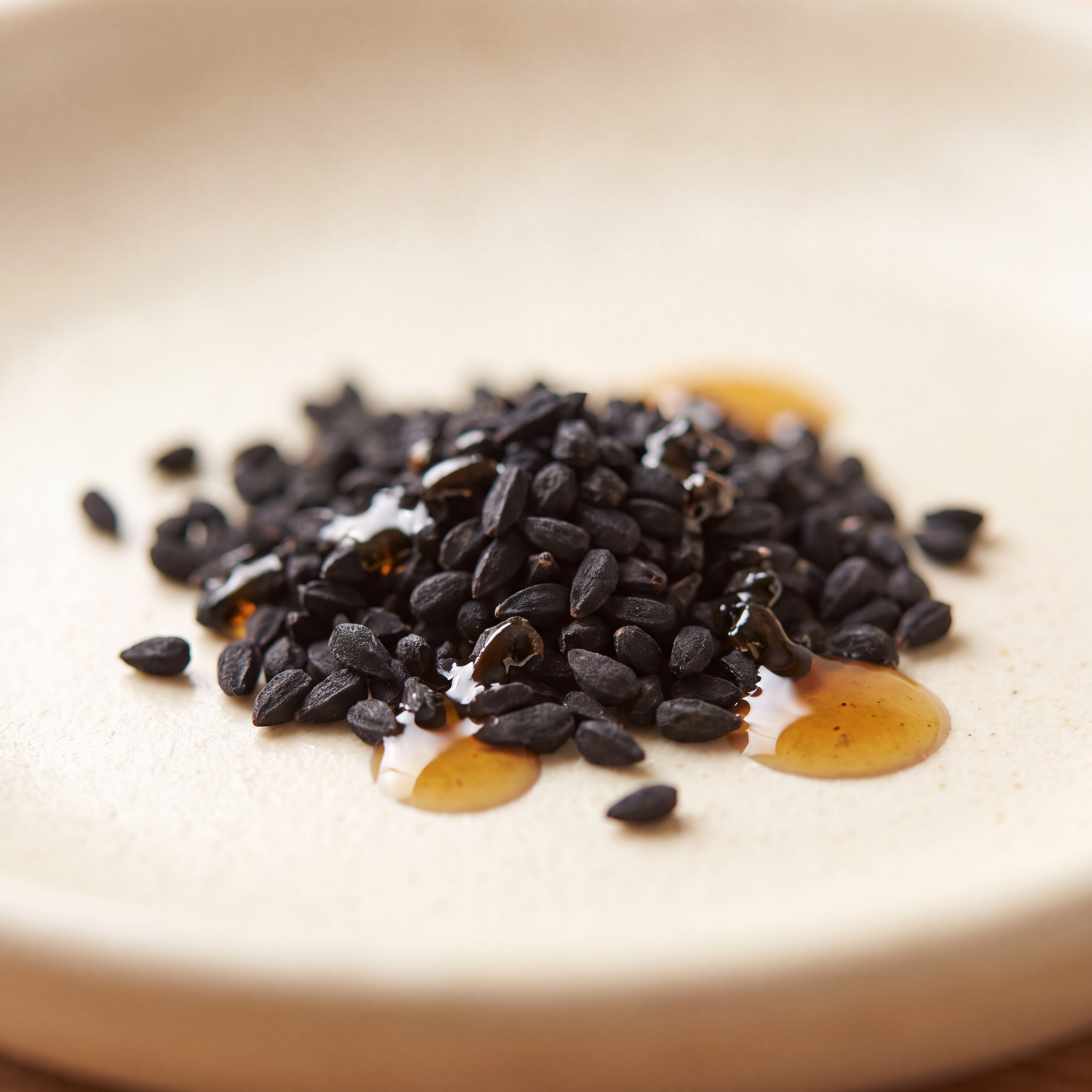 Black cumin (Nigella Sativa) seeds beside a bottle of cold-pressed black seed oil