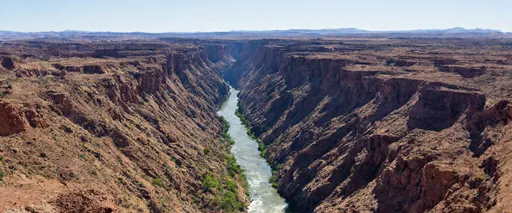 Prompt: This massive rift is located in New Mexico, USA, and features the iconic Rio Grande (Rio Bravo). Carving its way through the basalt flows of the Taos Plateau volcanic field, this area forms a breathtaking gorge. The Rio Grande, the fourth-largest river in North America, stretches from southern Colorado, winding through New Mexico, Texas, and eventually reaching its mouth in the Gulf of Mexico. Over millennia, the river’s relentless flow has shaped this dramatic landscape, highlighting the powerful forces of nature at work. The gorge is a striking example of how geology and water have sculpted the American Southwest.