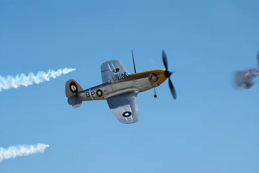 Prompt:  Inverted flight of a Supermarine Spitfire fighter, the iconic WWII aircraft. Defying gravity, its polished silver body gleams in the sunlight as it soars upside down, leaving a trail of white contrails against the clear blue sky. The distinctive sound of its Rolls-Royce Merlin engine roars in your ears, creating an unforgettable scene of power and agility.