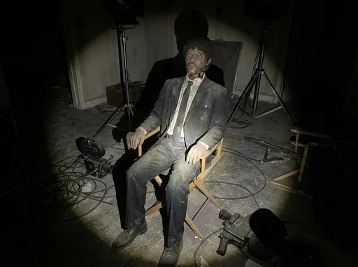 Prompt: Jules Winnfield sits rigidly in a wooden chair on a derelict apartment set, his animatronic body inert and heavy as the viewer’s flashlight beam reveals cracks in his synthetic skin and a lifeless stare frozen in place. His black suit hangs awkwardly, fabric worn thin at the shoulders, sleeves frayed, dust and grime embedded deep into the weave. Rusted metal joints are faintly visible at his neck and elbows. The floor around him is layered in dust, strewn with tangled cables, outdated camera rigs, and overturned light stands. Shot from chest height with a cinematic handheld angle, the flashlight is the only light source, carving harsh shadows into the decaying set while everything beyond the beam fades into blackness, hyper-realistic and eerily still.