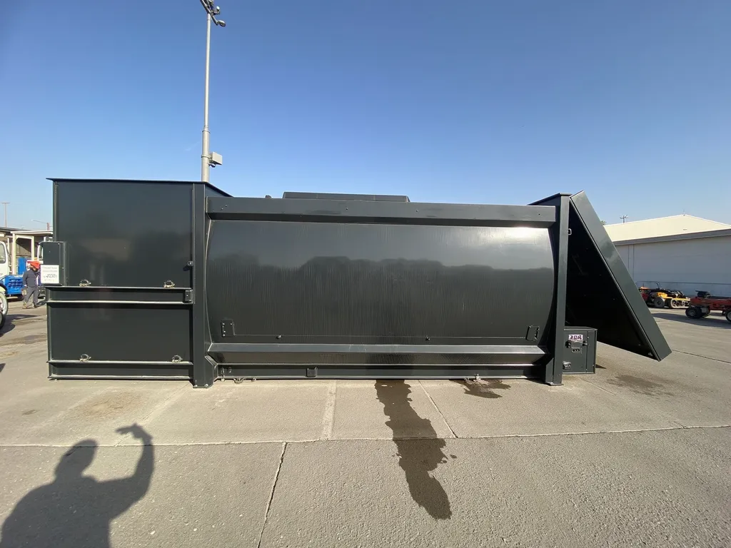 Prompt: Against a clear blue sky, a large, industrial-looking container dominates the scene, characterized by its sleek, dark gray metal surface that reflects sunlight. The container, positioned horizontally, features a slightly angled lid propped open, hinting at its functional design likely intended for storage or waste management. Surrounding the container is a dusty, paved area, with scattered machinery and equipment in the background, suggesting a busy construction or industrial site. The shadows cast by the daylight add depth to the image, while a faint sheen on the ground indicates recent activity, possibly from a spill or maintenance work. This snapshot conveys a sense of rugged efficiency in the industrial landscape.