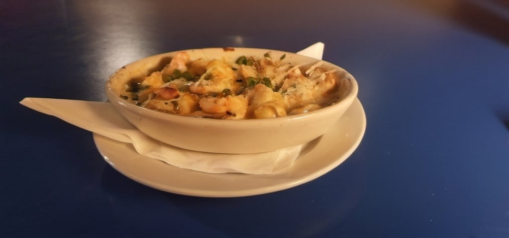 Prompt: A bowl of (Baked gnocchi, shrimp, tortellini, spicy cream sauce & green onions)  on napkin on a plate on a table. Steven M. Tilley, regionalism,  food photography.