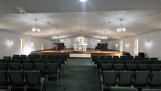 Prompt: Redesign this church. Remove all existing furniture and add all new green pattern chairs in the audience and 4 to the pulpit. Add  2 leather chairs to the pulpit. Add a new podium in the pulpit. Add a white communion table in the center of the church, near the front. Leave the 2 office doors on the right and left at the front of the church