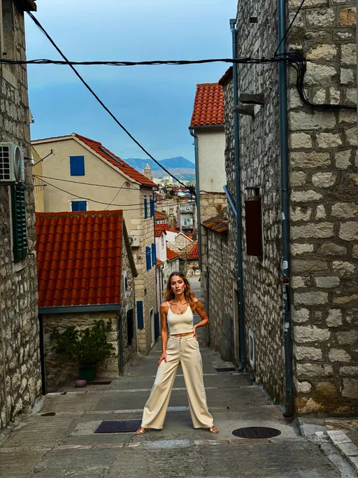 Prompt: @mNp5BVBkdiMVTOhH6ybH Ultra-realistic photo of Sol Amora, a 24-year-old Latina model with warm golden-tan skin, long honey-brown wavy hair that falls softly past her shoulders, caramel-brown eyes, full glossy lips, and sculpted but natural soft-glam makeup. Defined brows, subtle gold eyeshadow, and a smooth radiant complexion.She has a natural, genuine smile, relaxed expression, and confident posture.Outfit: A stylish cream-colored ribbed knit tank top paired with high-waisted light beige wide-leg trousers. Minimal gold jewelry: small gold hoop earrings, a thin gold chain necklace, and a delicate gold bracelet. Neutral-tone makeup that enhances her natural beauty.Hair, face, and styling all match her signature warm, glowing Latina aesthetic.