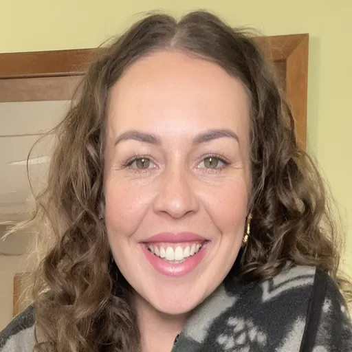 Prompt: A woman with curly, voluminous hair beams with a warm smile against a vibrant green background. She is wearing a blue top adorned with light-colored floral patterns, accentuating her cheerful disposition. Her makeup is natural, enhancing her features while she sports small, elegant earrings. The overall scene exudes an inviting and friendly atmosphere, suggesting a moment of joy or celebration captured in a bright, joyful style.