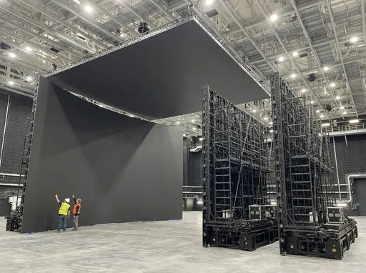 Prompt: use  @image01 and background, add 4 LED modular walls  that stand 26 feet in height.  Connect 2 of the walls like in @image05 and space out the other 2 like they are about to be connected. Use  @image02, @image03, @image04, as reference of walls front back and side. Make sure walls are 26 feet tall. Add square LED ceiling over the top like in @image05. Have square LED ceiling  touching top of walls like @image05. Have 1 to 2 workers at the base of them looking up at them for placement. 