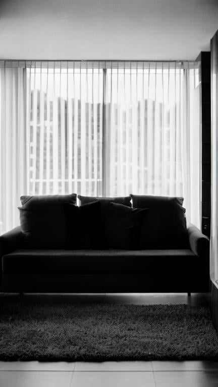 Prompt: A wide view of a living room, 30-year-old casual woman in her birthday suit sitting on a couch at night, au naturel, applying body lotion, late evening, sharp jawline, interesting face, dimples, sinister mood, arms crossed, lowkey dramatic lights, ilford hp5 1600, shot for penthouse, photo by helmut newton, knees wide apart