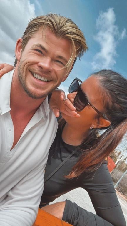 Prompt: a man and woman sitting on a bench together smiling at the camera with a sky background and clouds in the background, Aramenta Dianthe Vail, rasquache, love, a picture, Chris Hemsworth smiling