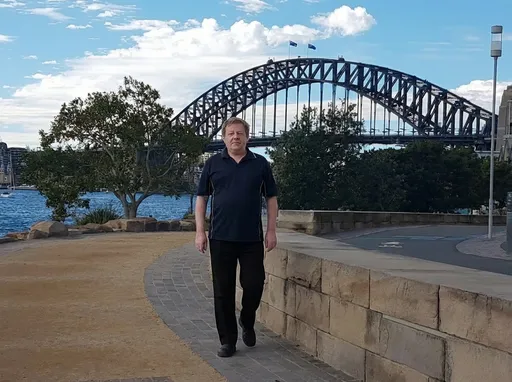 Prompt: Use image 1 as the environment reference: Barangaroo Reserve, featuring sandstone elements, greenery, and Sydney Harbour in the background.

Use image 2 as the avatar reference: MR A.J., preserving his identity exactly as shown.

Place MR A.J. into the Barangaroo environment from image 1.

Animate the scene into a 10-second photorealistic video.

MR A.J. is walking slowly and naturally toward the camera, moving in a straight line. His pace is calm and relaxed, like a casual everyday walk.

Walking motion is fully human and realistic:

heel-to-toe steps

natural leg movement

relaxed arm swing at his sides

subtle body sway

gentle breathing

His facial expression remains neutral to mildly friendly, relaxed and natural. No exaggerated smile.

Hair, face shape, skin texture, body proportions, and clothing remain unchanged and realistic, with no beautification or stylisation.

Lighting matches the Barangaroo scene with natural daylight, soft and even.

The camera remains completely static and eye-level while MR A.J. approaches. No panning, zooming, or shaking.

The video should feel like natural lifestyle B-roll, calm, confident, and authentic.

No talking. No speech. No audio.

Negative Prompt:

No walking backward
No side stepping
No stopping and starting
No exaggerated stride
No stiff or robotic gait
No sliding feet
No teleporting
No camera movement
No panning
No zooming
No drifting
No facial changes
No beautified face
No stylised hair
No identity drift
No flickering
No jittering
No blur
No artifacts
No audio
No sound
No text
No logos
No watermarks