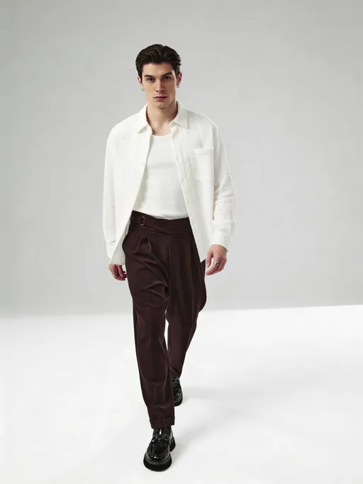 Prompt: Кадр от уровня талии до обуви. В кадре — наша эталонная мужская модель в наших тёмно-коричневых брюках из плотной матовой костюмной ткани с шоколадно-бордовым подтоном.

Брюки:
высокая посадка; широкий асимметричный пояс с запахом; сбоку встроенный поясной хлястик с металлической прямоугольной пряжкой и пуговицей в тон; спереди две глубокие складки, формирующие объём в области бёдер; свободный расслабленный силуэт; штанины плавно сужаются к низу; длина укороченная с аккуратным фиксированным подворотом.

Стилизация (ОБЯЗАТЕЛЬНО):
– светлая молочно-белая рубашка прямого кроя из фактурной ткани, расстёгнута
– под рубашкой — базовая молочно-белая / айвори майка, без принтов и декора
– рукава рубашки свободные, естественная посадка

Обувь:
чёрные кожаные лоферы классической формы, гладкая кожа, без логотипов и декора.


Поза:
Корпус прямо перед камерой 
Кадр от талии до обуви 
модель делает лёгкий шаг вперёд в камеры; одна нога выдвинута, ткань брюк красиво драпируется; поза живая, естественная, editorial.

Фон:
белый однотонный студийный фон с мягкими естественными тенями от ног; чистый дневной свет; без лишних предметов.

Стиль кадра:
премиальный fashion / editorial, clean minimalism, акцент на посадке брюк, складках и поясе; реалистичная цветопередача, высокая детализация ткани, ultra-realistic, high quality, sharp focus.