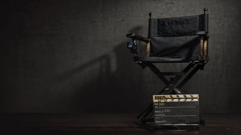 Prompt: Realistic style image of a director's chair on the left of the image with a film slate, medieval style, dark background, rocky black background, Ancell Stronach, art, filmic, stock photo, detailed wood texture, professional lighting , cinematic atmosphere, high quality, photo-realistic, dark tones, iconic film equipment,