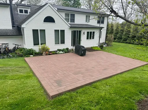 Prompt: Create a 25x35 brick patio off the back of a white, remodeled, cape style house.