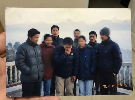 Prompt: Generate an image of an spoiled photograph due to coughing. the photograph was supposed to capture 6-7 nepalese college friends at a beautiful scene in Nagarkot of Nepal. One of the friend in the photo should be coughing