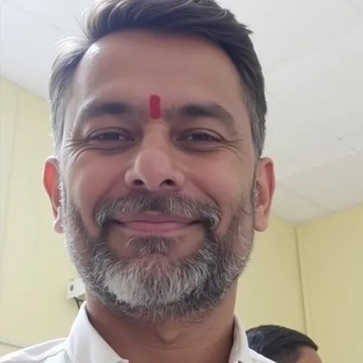 Prompt: A man with a light beard and neatly groomed appearance gazes into the camera, his expression calm and composed. He sports a traditional red mark on his forehead, indicative of cultural or religious significance. The soft lighting of the indoor setting, highlighted by gentle yellow walls, creates a warm and inviting atmosphere. His slight smile suggests friendliness, and the focus on his face contrasts with the blurred background, emphasizing his presence. Overall, the image conveys a sense of approachability and warmth.
