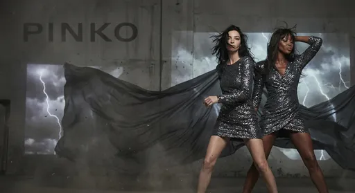 Prompt: Visualize Maria Carla Boscono and Naomi Campbell in a windy studio campaign by Pinko posing artistically and fashion with mini dress sequinned. 
The campaign is dark, windy and with thunderbolt and lightning in a ton sur ton with dark grey sequinned.
The models pose fiercely in this studio 