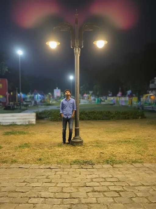 Prompt: A young man stands casually beside an ornate street lamp in a vibrant park, illuminated by the warm glow of the lamp and additional nearby lights that contribute to the nighttime ambiance. Dressed in a light blue shirt and fitted jeans, he gazes upwards, perhaps lost in thought or admiring the surroundings, with a relaxed posture that suggests a moment of leisure. The background features hints of colorful decorations and greenery, creating a lively atmosphere, while the uneven stone pavement leading up to him adds texture to the scene. The overall mood is one of relaxation and contemplation, enhanced by the soft lighting and the pleasantly darkened sky, which hints at a bustling yet serene evening.