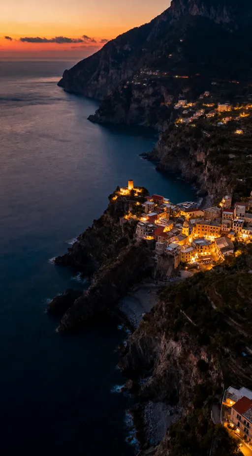 Prompt: Ultra realistic aerial 8K photograph of a massive coastline during rich evening sunset, glowing villages along the cliffs, atmospheric depth, deep navy and warm amber tones, authentic luxury travel photography
