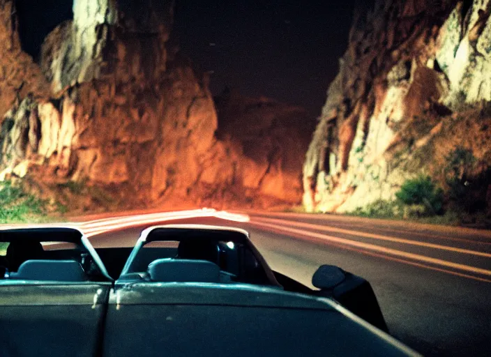 Image similar to pov a couple is the front seat, headlights of a car illuminate a strange dark canyon road, it's the dead of night, in a distance the bright city lights glow, cinematic, cinestill