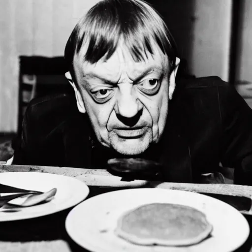 Image similar to mark e smith sitting at a table eating a big stack of pancakes, fork and knife in hand, drooling and licking his lips, photograph