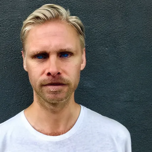 Image similar to full face color photograph of a 40 year old very handsome white man with very short, wavy, light blond hair and very small slanted blue eyes, dressed in a white t shirt, gray shorts and black socks, with very thin lips, with a straight nose and blond stubble on his oval face, and pale skin. He resembles a lion.