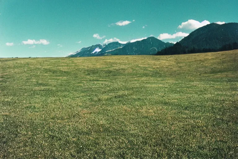 Prompt: film color photography, small mirror in distance, long view of green lawn, no focus, mountains in distance, 35mm