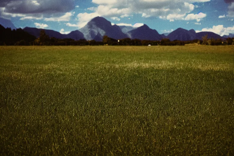 Image similar to film color photography, green lawn, small mirror reflected clouds, no focus, mountains in distance, 35mm