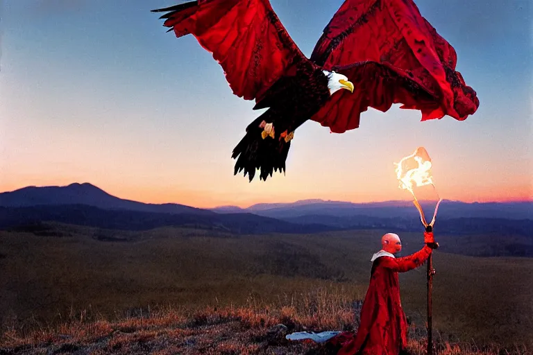 Image similar to at Dusk a witch woman dressed in an elaborate tattered cloak with hood, stands overlooking a mountain range as she holds up a lit and burning red signal flare. An american bald eagle flies towards her. Portrait by annie Liebowitz.