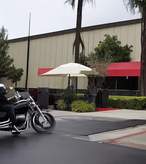 Image similar to Andy Richter is dressed in a black suit and a red necktie and riding a motorcycle into a studio lot. The studio lot is filled with Soundstages and movie trailers. It is a bright afternoon and overcast.