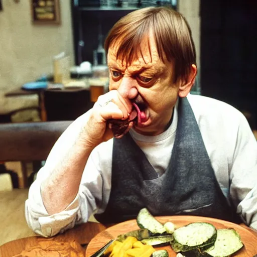 Image similar to mark e smith sitting at a table eating a big pile of vegetables, fork and knife in hand, drooling and licking and smacking his lips, photograph