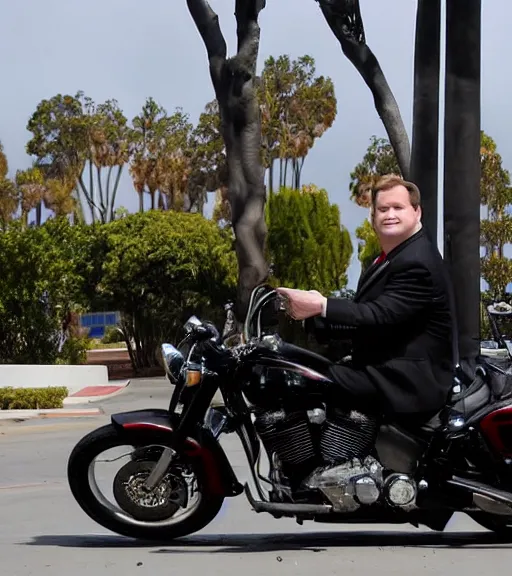 Image similar to Andy Richter is dressed in a black suit and a red necktie and riding a motorcycle into a studio lot. The studio lot is filled with Soundstages and movie trailers. It is a bright afternoon and overcast.