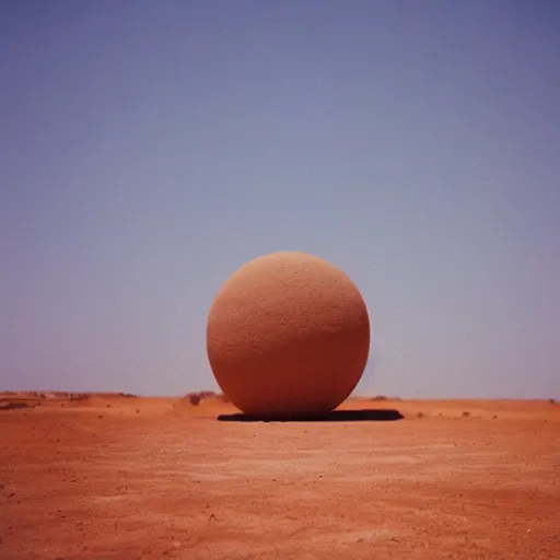 Image similar to a Non-Euclidean orb-like clay building sitting in the desert, vintage photo, beautiful cinematography, blue sky, film grain, extreme wide shot, far away, symmetrical, in the distance, James Turrell