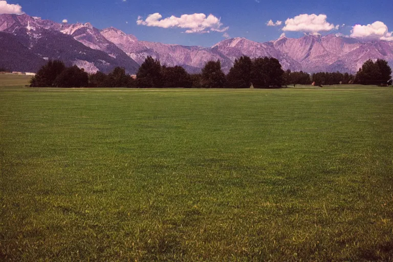 Image similar to film color photography, small mirror in distance, long view of green lawn, no focus, mountains in distance, 35mm