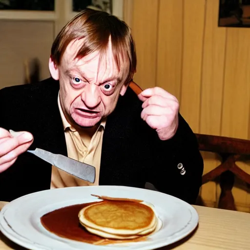 Prompt: mark e smith sitting at a table eating a big stack of pancakes, fork and knife in hand, drooling and licking his lips, photograph