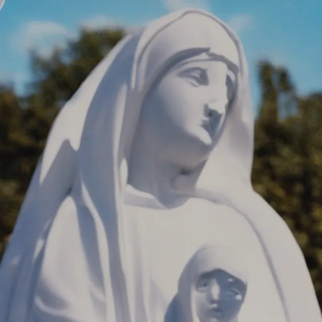 Prompt: closeup of white mother mary statue pictured slightly from below, clear sky with blue clouds in background, vintage polaroid