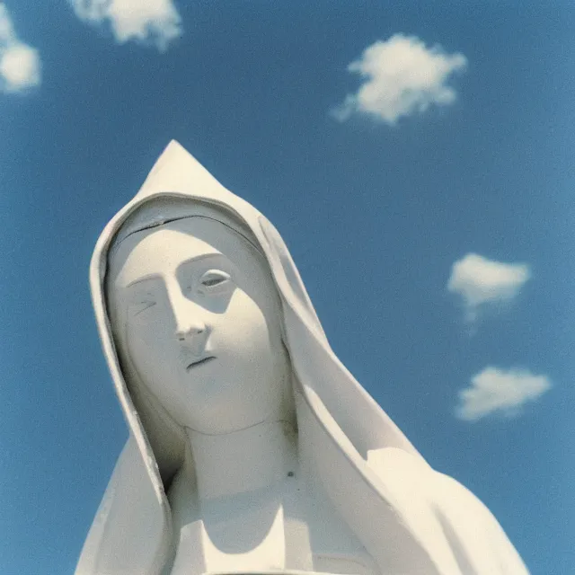 Image similar to closeup of white mother mary statue pictured slightly from below, clear sky with blue clouds in background, vintage polaroid